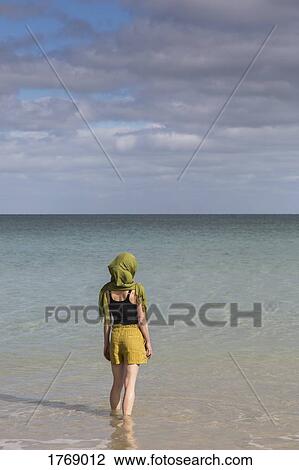 Stock Image - Serene woman with headscarf wading in sunny ocean. Fotosearch