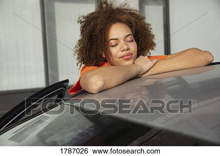 Stock Photograph - Serene young woman leaning on car. Fotosearch