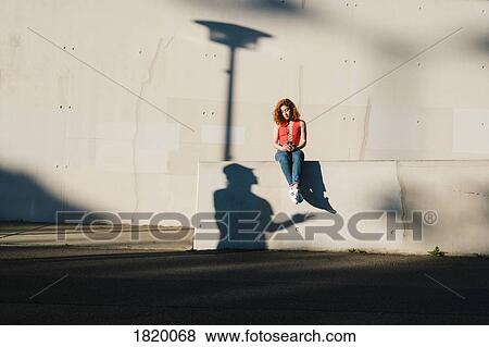 Shadow looking up at young woman using smart phone on urban wall View Large Photo Image Stock Photo - Shadow looking up at young woman using smart phone on urban wall. Fotosearch