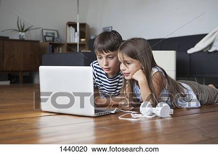 Siblings using laptop while lying on hardwood floor at home View Large Photo Image Stock Image - Siblings using laptop while lying on hardwood floor at home. Fotosearch