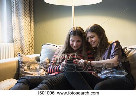 Siblings using mobile phone on sofa at home View Large Photo Image Stock Photograph - Siblings using mobile phone on sofa at home. Fotosearch