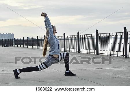 Stock Image - Side view of female athlete stretching on promenade. Fotosearch