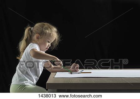 Stock Image - Side view of girl drawing on paper at table against black background. Fotosearch