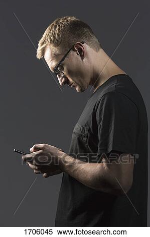 Side view of man using mobile phone while standing against gray background View Large Photo Image Stock Photography - Side view of man using mobile phone while standing against gray background. Fotosearch