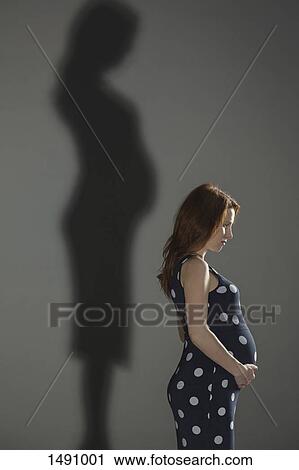 Stock Image - Side view of pregnant woman with shadow on gray background. Fotosearch