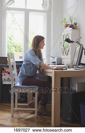 Side view of smiling young woman using computer at table in room View Large Photo Image Stock Photo - Side view of smiling young woman using computer at table in room. Fotosearch