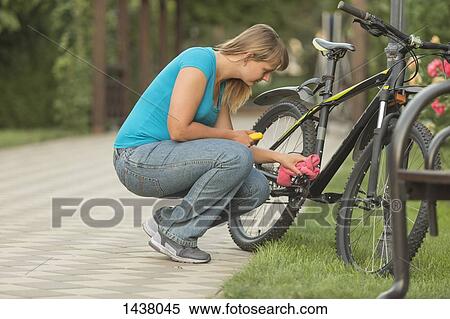Side view of woman repairing bicycle in park View Large Photo Image Stock Photography - Side view of woman repairing bicycle in park. Fotosearch