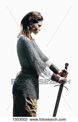 Stock Image - Side view of woman wearing chain mail with sword standing against white background. Fotosearch