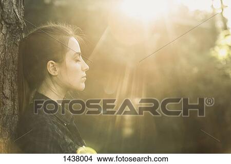 Side view of young woman with eyes closed enjoying sunlight at park View Large Photo Image Picture - Side view of young woman with eyes closed enjoying sunlight at park. Fotosearch