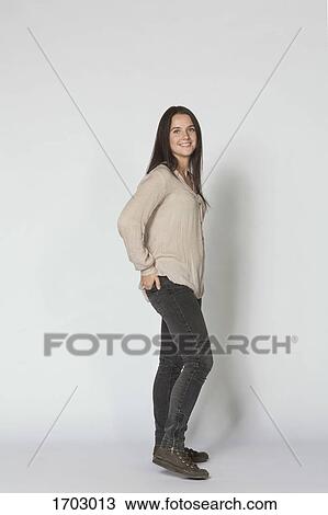 Stock Image - Side view portrait of smiling beautiful woman standing against white background. Fotosearch