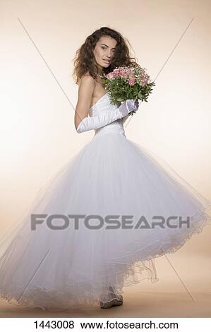 Stock Photo - Side view portrait of young bride holding bouquet against colored background. Fotosearch