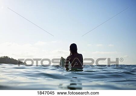 Silhouette female surfer straddling surfboard, waiting in sunny blue ocean View Large Photo Image Stock Photography - Silhouette female surfer straddling surfboard, waiting in sunny blue ocean. Fotosearch