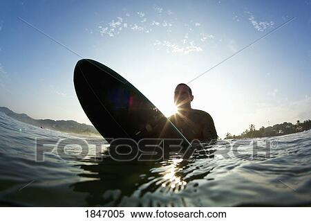 Silhouette male surfer straddling surfboard in sunny ocean View Large Photo Image Stock Photography - Silhouette male surfer straddling surfboard in sunny ocean. Fotosearch