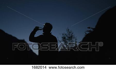 Silhouette man drinking water from bottle while standing on mountain at night View Large Photo Image Picture - Silhouette man drinking water from bottle while standing on mountain at night. Fotosearch