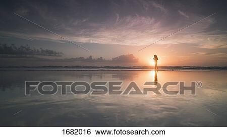 Stock Photograph - Silhouette woman at sea shore against cloudy sky during sunset, Daytona, Florida, USA. Fotosearch