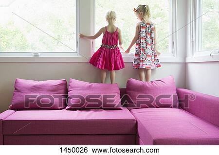 Sisters standing on pink sofa by window at home View Large Photo Image Stock Photograph - Sisters standing on pink sofa by window at home. Fotosearch