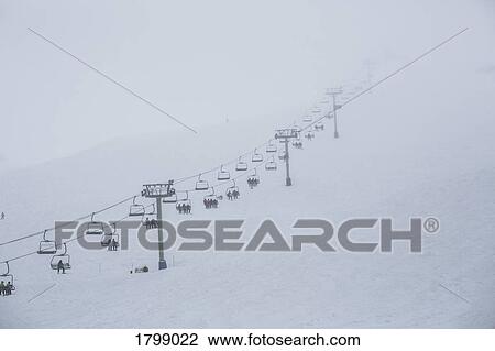 Skiers riding ski resort chair lift up mountainside View Large Photo Image Stock Image - Skiers riding ski resort chair lift up mountainside. Fotosearch