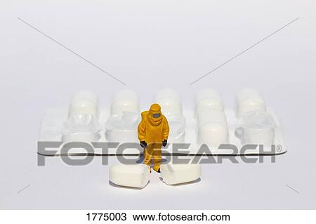 Stock Image - Small scientist in clean suit examining white tablet from blister pack. Fotosearch