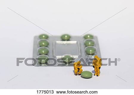 Stock Image - Small scientists in clean suits examining green pill from blister pack. Fotosearch