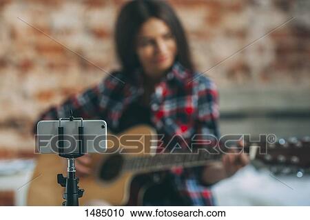 Smart phone in monopod with woman playing guitar in background at home View Large Photo Image Stock Image - Smart phone in monopod with woman playing guitar in background at home. Fotosearch