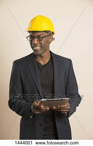 Smiling architect looking away while holding digital tablet against colored background View Large Photo Image Stock Image - Smiling architect looking away while holding digital tablet against colored background. Fotosearch