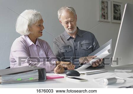 Smiling business colleagues discussing over documents at desk in office View Large Photo Image Stock Image - Smiling business colleagues discussing over documents at desk in office. Fotosearch