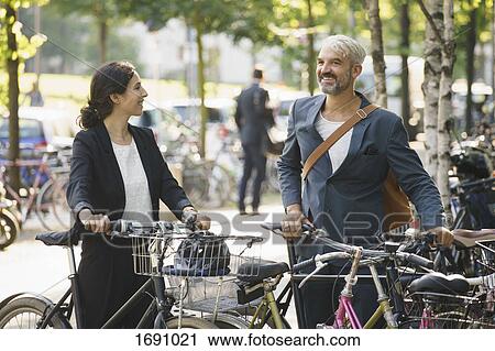 Smiling colleagues talking while standing with bicycles at parking lot View Large Photo Image Stock Image - Smiling colleagues talking while standing with bicycles at parking lot. Fotosearch