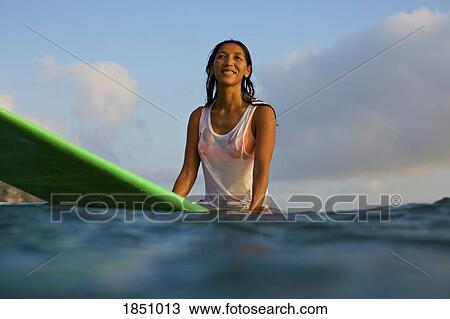 Stock Image - Smiling, confident female surfer waiting on surfboard in ocean. Fotosearch