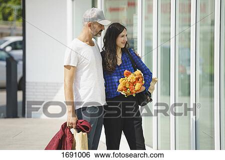 Smiling couple standing by glass building on sunny day View Large Photo Image Stock Photograph - Smiling couple standing by glass building on sunny day. Fotosearch