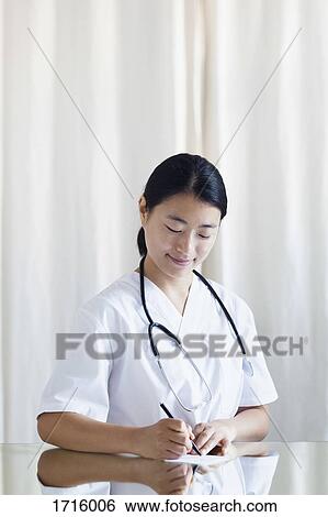 Smiling female doctor writing prescription at table in clinic View Large Photo Image Stock Photograph - Smiling female doctor writing prescription at table in clinic. Fotosearch