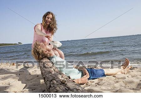 Stock Image - Smiling friend feeding cherry to young man while relaxing at beach. Fotosearch