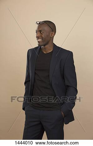 Smiling man looking away while standing with hands in pockets against colored background View Large Photo Image Stock Image - Smiling man looking away while standing with hands in pockets against colored background. Fotosearch