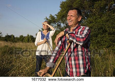 Smiling mature couple with equipment standing at farm on sunny day View Large Photo Image Stock Image - Smiling mature couple with equipment standing at farm on sunny day. Fotosearch