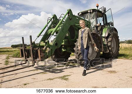 Smiling mature woman walking by agricultural machinery at farm against sky View Large Photo Image Stock Photograph - Smiling mature woman walking by agricultural machinery at farm against sky. Fotosearch