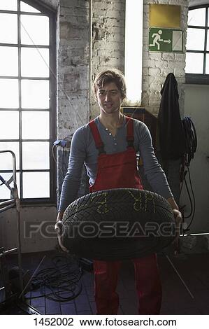 Smiling mechanic holding tire at garage View Large Photo Image Stock Image - Smiling mechanic holding tire at garage. Fotosearch