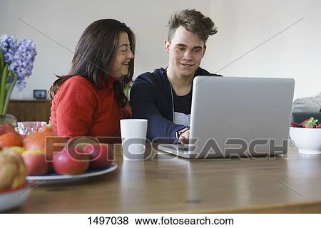 Smiling mother and son using laptop on table at home View Large Photo Image Stock Photo - Smiling mother and son using laptop on table at home. Fotosearch
