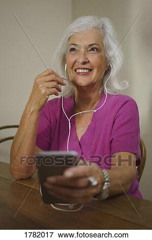 Stock Photo - Smiling senior woman listening to music with headphones and mp3 player. Fotosearch