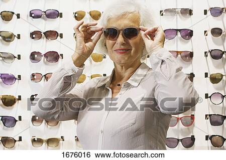 Smiling senior woman wearing sunglasses while standing at store View Large Photo Image Stock Photograph - Smiling senior woman wearing sunglasses while standing at store. Fotosearch