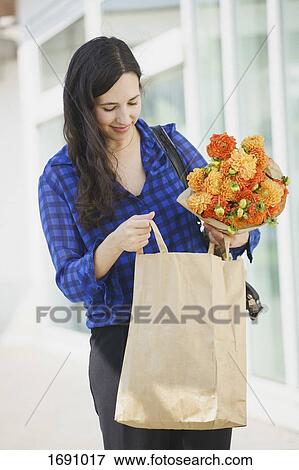Smiling woman holding flowers bouquet while looking in paper bag View Large Photo Image Stock Photo - Smiling woman holding flowers bouquet while looking in paper bag. Fotosearch