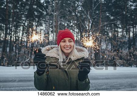 Stock Image - Smiling woman holding sparklers during winter. Fotosearch