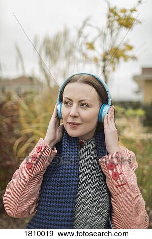 Smiling woman listening to music with headphones outside View Large Photo Image Stock Photo - Smiling woman listening to music with headphones outside. Fotosearch