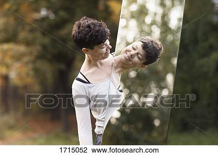 Smiling woman looking in mirror while standing at park View Large Photo Image Stock Image - Smiling woman looking in mirror while standing at park. Fotosearch