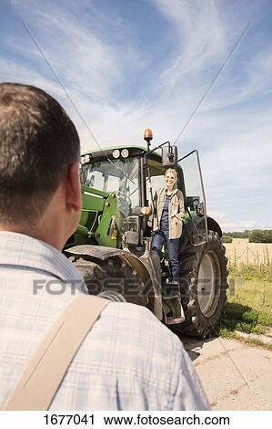 Smiling woman standing on tractor while looking at man against sky View Large Photo Image Stock Image - Smiling woman standing on tractor while looking at man against sky. Fotosearch