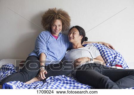 Picture - Smiling young couple resting on bed against white wall at home. Fotosearch