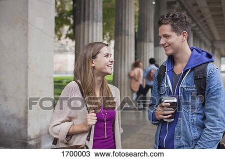Stock Image - Smiling young friends talking while standing against columns. Fotosearch