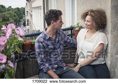 Smiling young friends talking while sitting by wall in balcony View Large Photo Image Stock Image - Smiling young friends talking while sitting by wall in balcony. Fotosearch