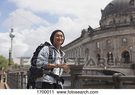 Stock Image - Smiling young male tourist standing with map by railing against Bode Museum, Berlin, Germany. Fotosearch