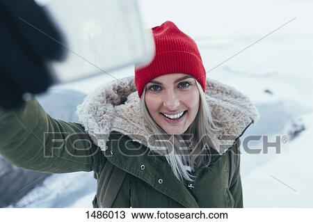 Stock Image - Smiling young woman taking selfie on smart phone during winter. Fotosearch