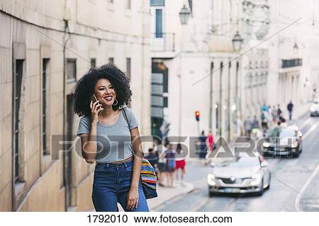 Stock Image - Smiling young woman talking on smart phone on urban street, Lisbon, Portugal. Fotosearch