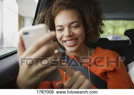 Stock Photo - Smiling young woman using smart phone in car. Fotosearch